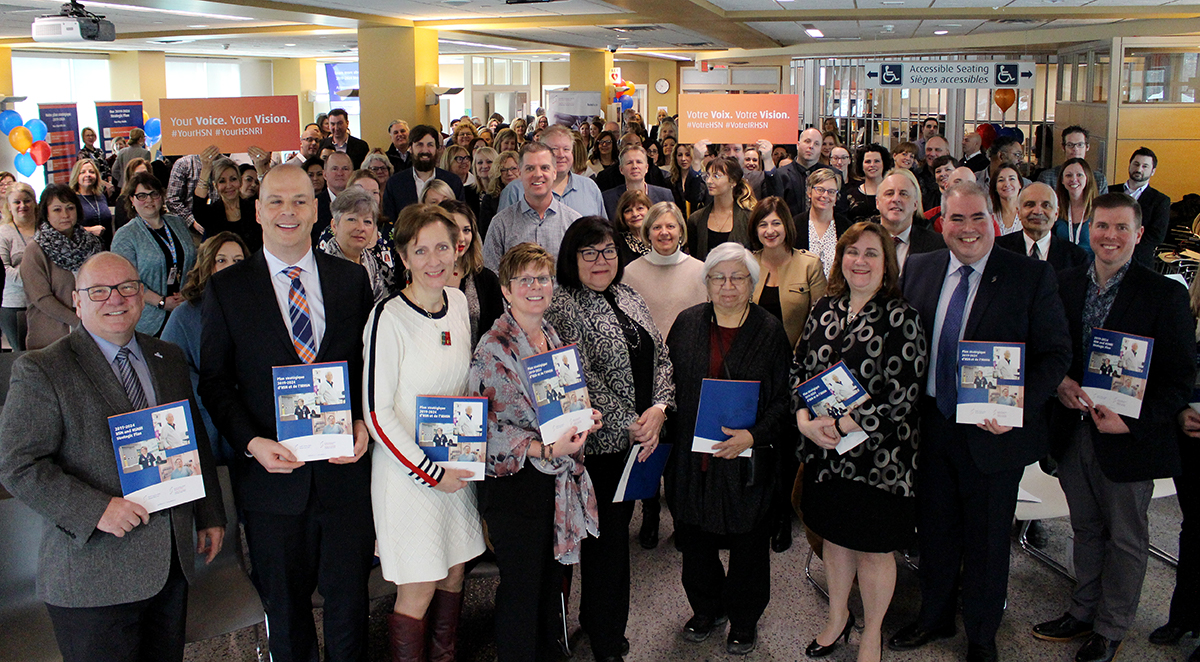 Crowd of people at Health Sciences North's cafeteria in Sudbury, Ontario, celebrating the launch of HSN and HSNRI's 2019-2024 strategic plan.